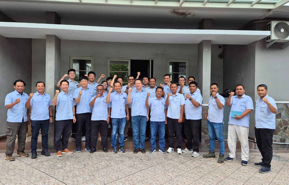 A large group of SNG employees in light blue uniforms pose outside a building, raising their fists.