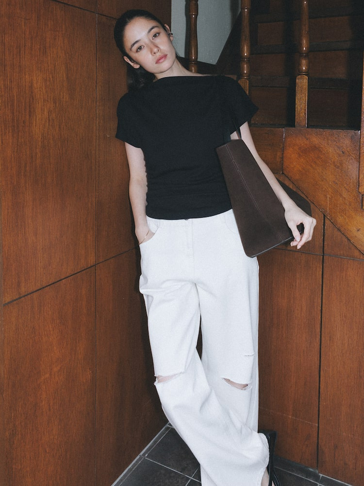 Model wearing The Aperture’s Keith Boat Neck Top - Black with wide-leg distressed white pants and a dark brown clutch.