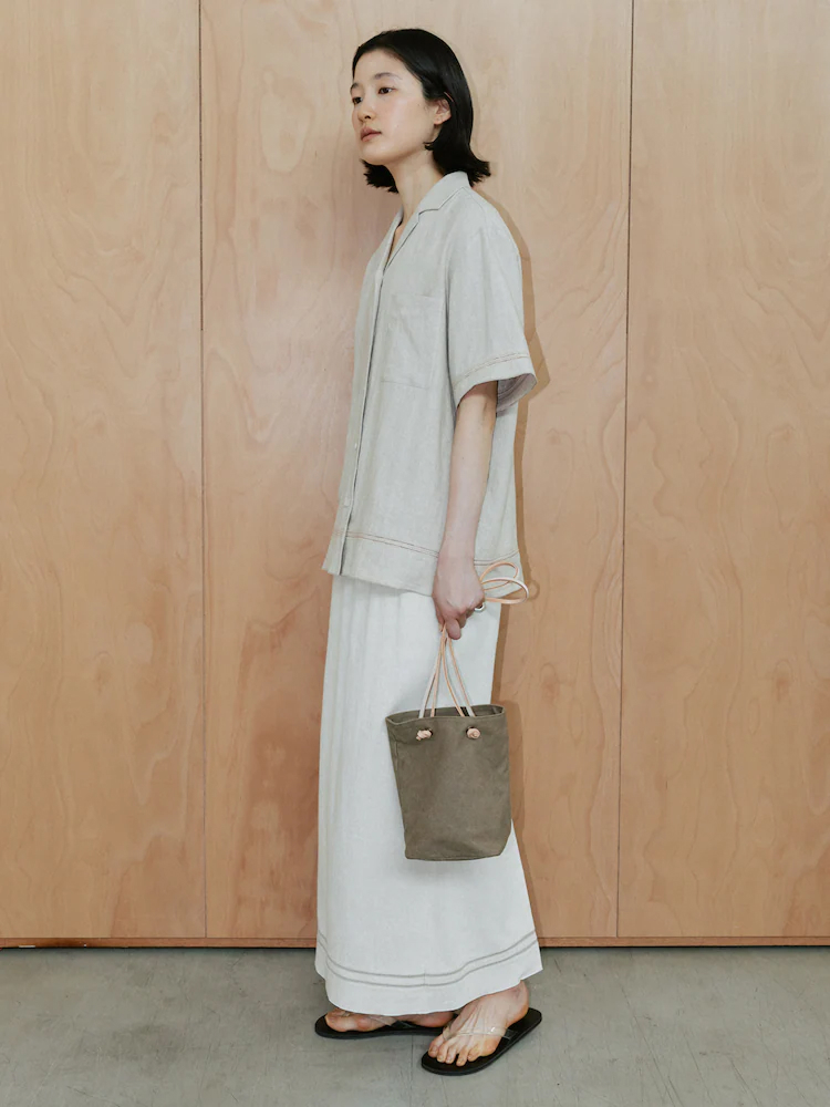Model wearing The Aperture’s Loic H Line Skirt - Ivory with a matching short-sleeved jacket, flat sandals and a taupe handbag.