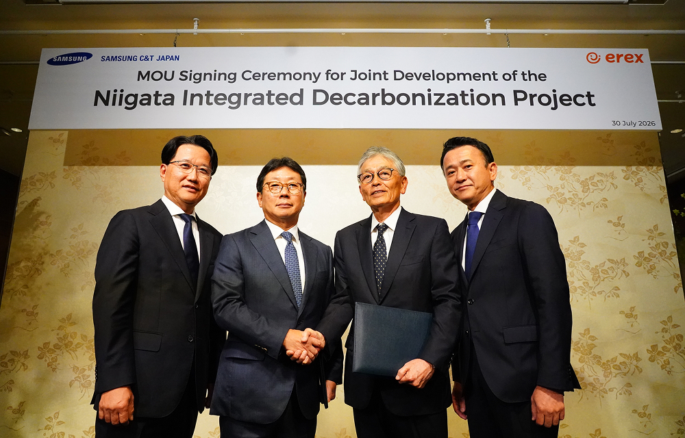 Four company representatives in suits stand together at an MOU signing ceremony for the Niigata Integrated Decarbonization Project, with two representatives shaking hands in front of a Samsung C&T Japan and eRex event banner.