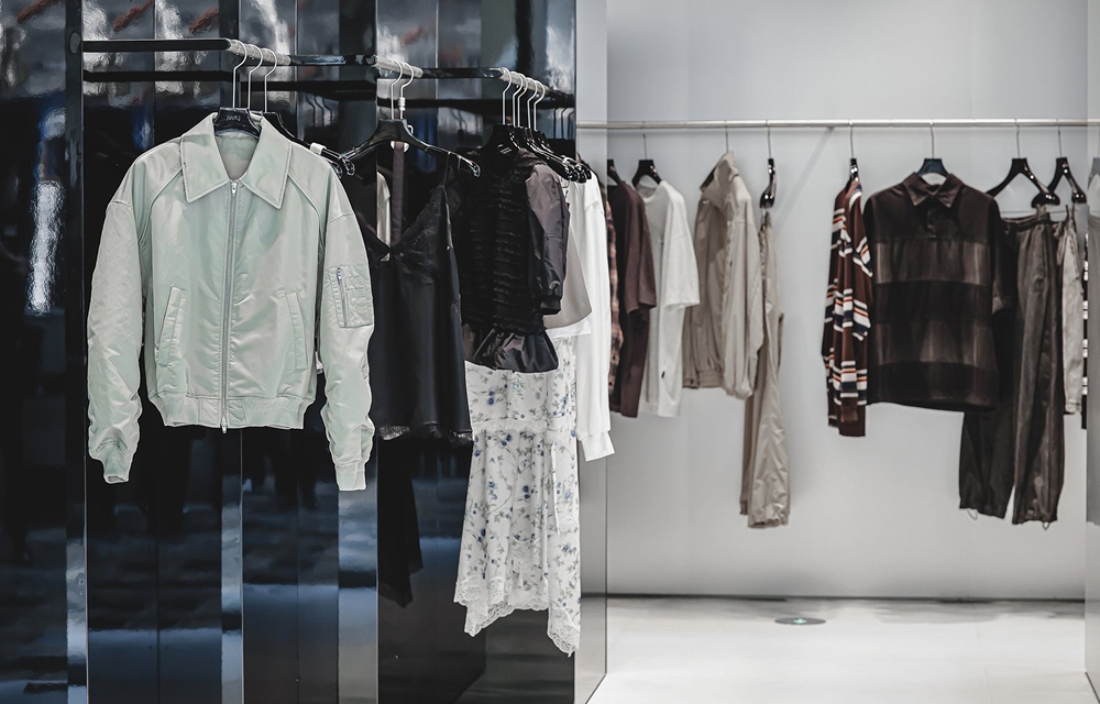 Mint bomber jacket, floral skirt, striped knitwear, and dark garments displayed on black and silver rails inside the JUUN.J Beijing store.