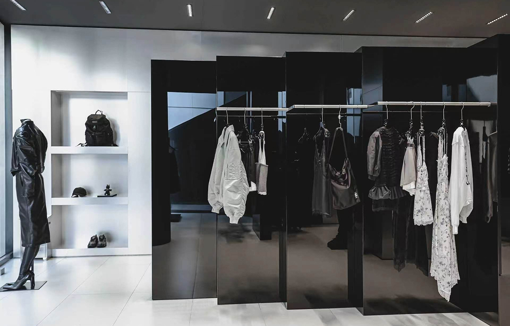 Interior of the JUUN.J Beijing store featuring glossy black display structures, silver clothing rails, and black-and-white garments.