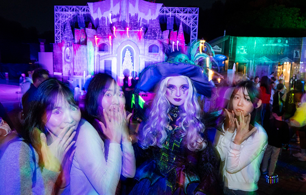 Visitors posing with costumed horror performers beneath purple and green lighting at Blood City Zero.