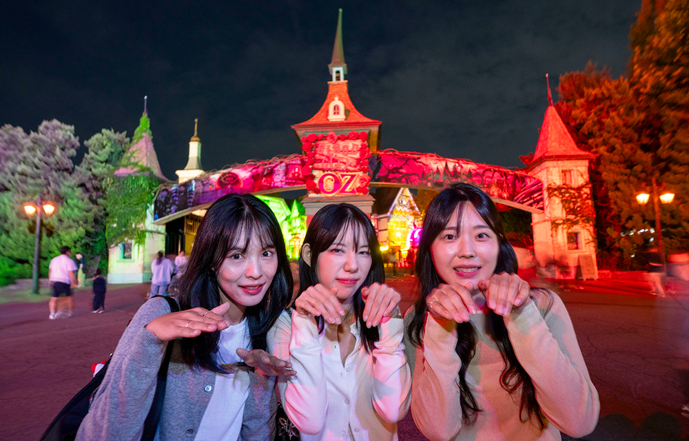 Three visitors posing together in the illuminated Blood City Zero plaza at night.