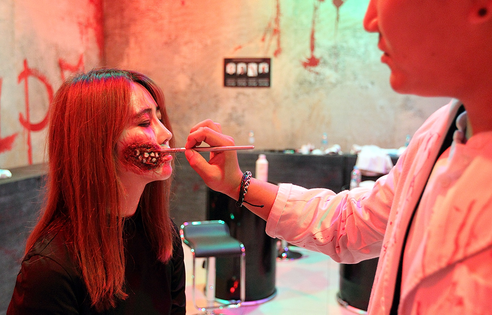A makeup artist applies red special-effects makeup to a visitor at the Zombie Makeup Salon.
