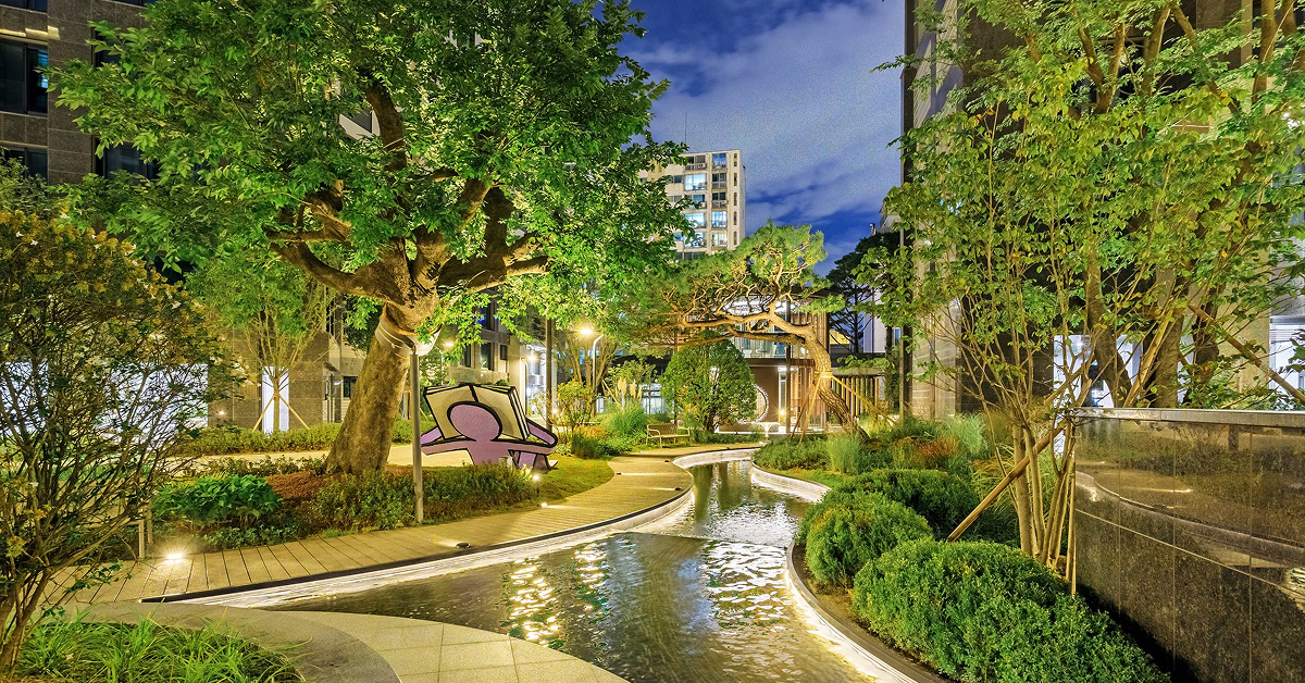 Wind Library Garden at Raemian One Perla, featuring lush landscaping, mature trees, curved walking paths, and a narrow waterway winding through the residential garden.