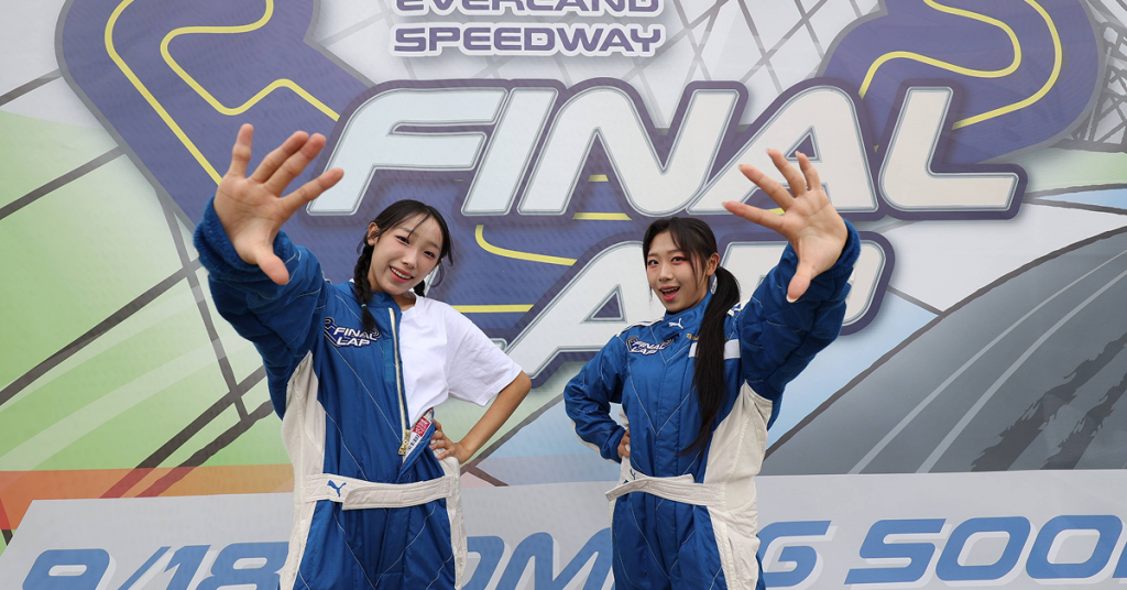 Two visitors in blue racing suits pose in front of a colorful Final Lap promotional wall at Everland