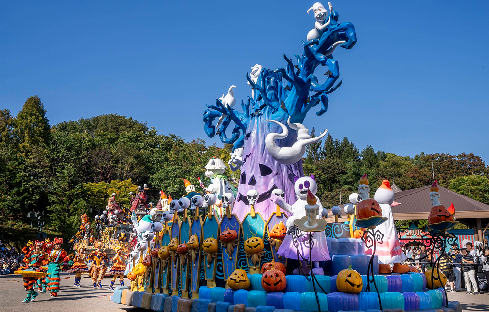 A large blue-and-purple float decorated with pumpkins and skeleton characters stands along Everland’s parade route.