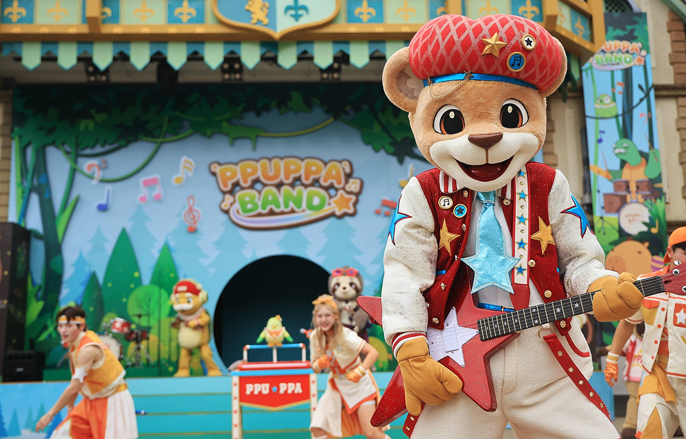A costumed animal character holds a red guitar on the Ppuppa Band stage, with dancers performing behind.