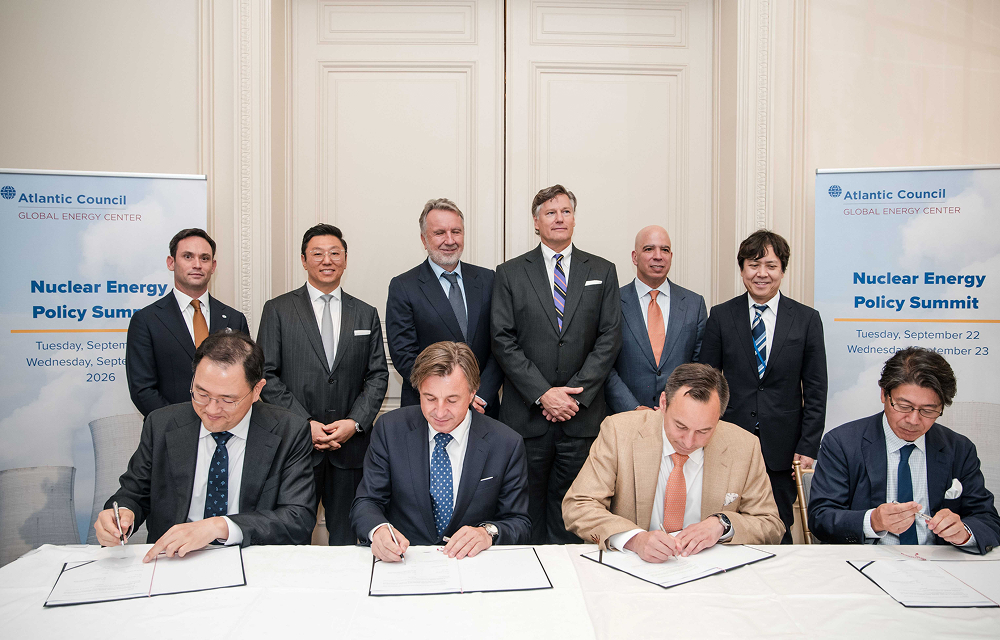 Four executives sign documents at a table during the MOU ceremony in New York, with six representatives standing behind them. Seated from left are Jung Wook Kim of Samsung C&T, Rafał Kasprów of SGE, Scott Strazik of GE Vernova and Yasuhiro Takeuchi of Hitachi.