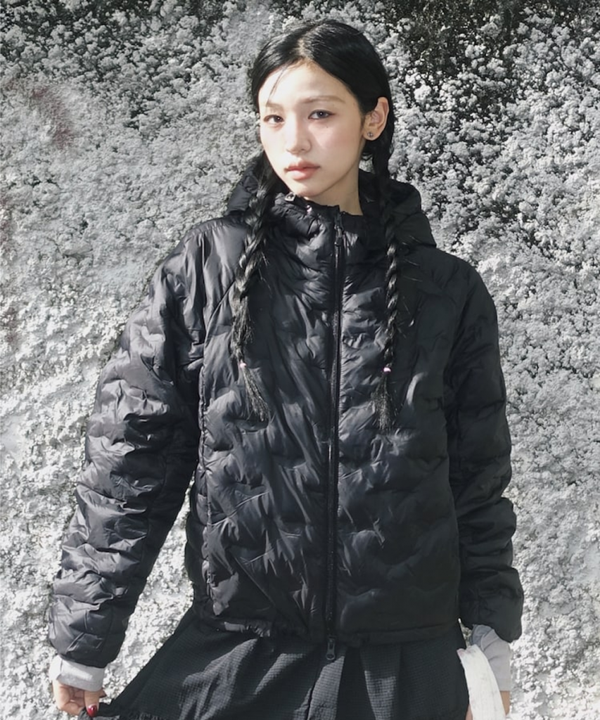 A model wears a light gray hooded puffer jacket with dark wide-leg pants in an indoor setting.