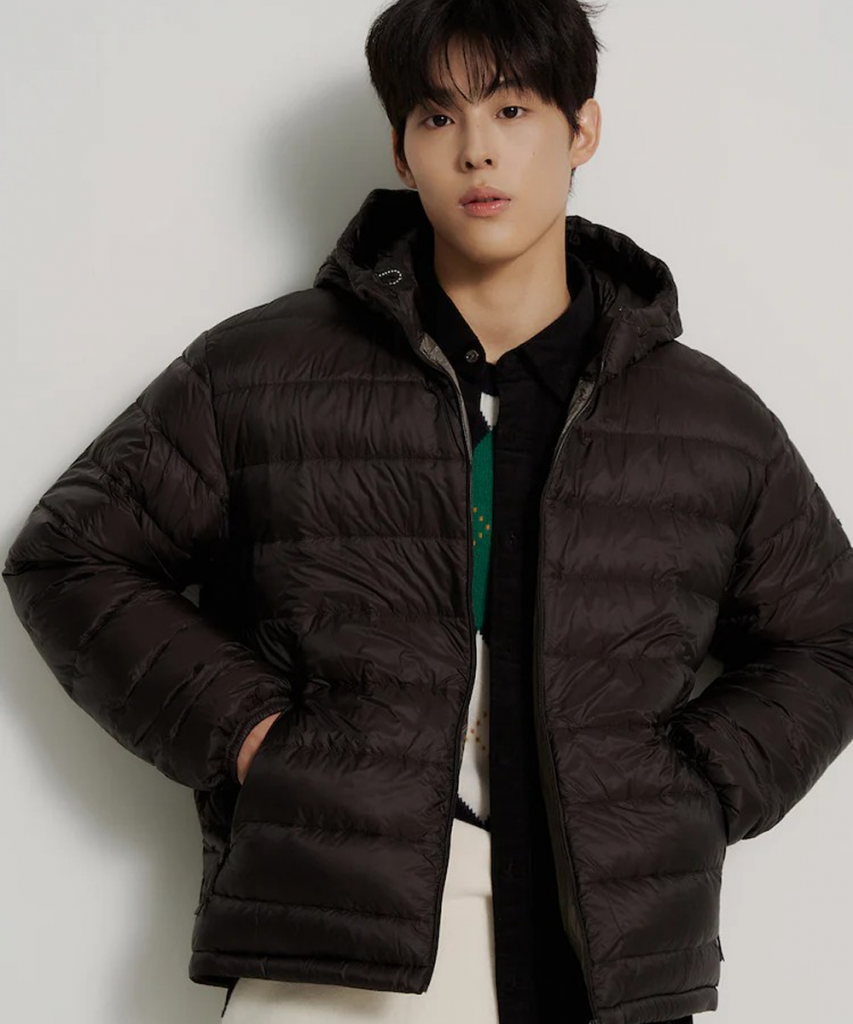A male model wears a black hooded puffer jacket layered over a dark top and light-colored pants against a neutral studio background.