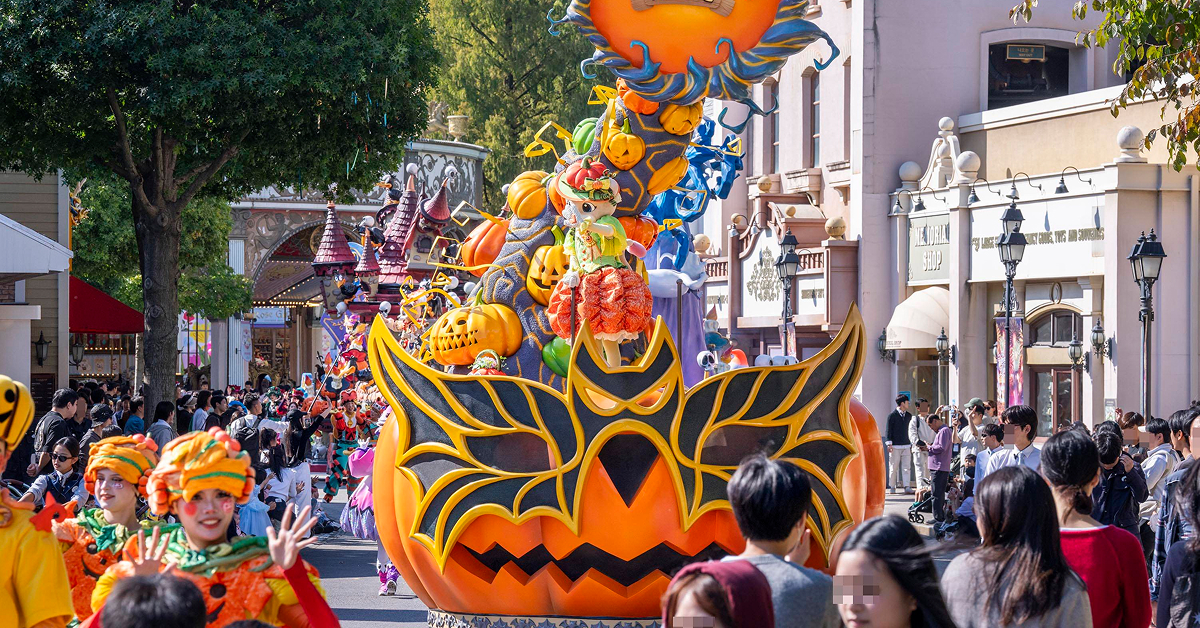 An orange pumpkin-themed float leads costumed performers along an outdoor parade route at Everland.
