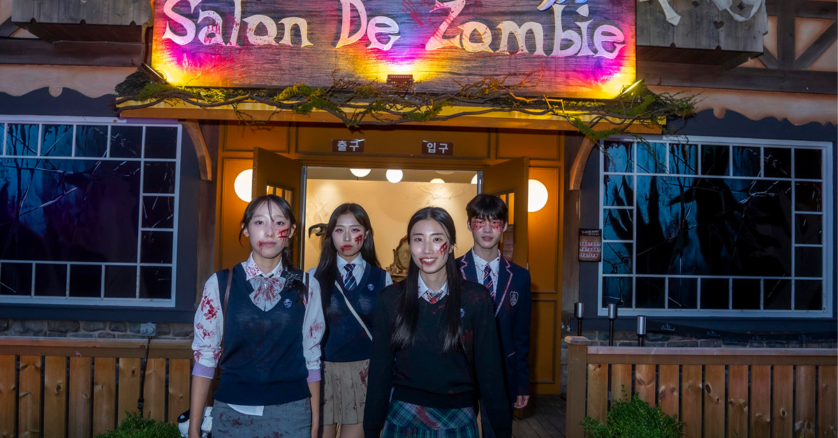 Four performers with zombie-style face makeup pose outside Everland’s Salon De Zombie beneath oversized monster hands and an illuminated sign.