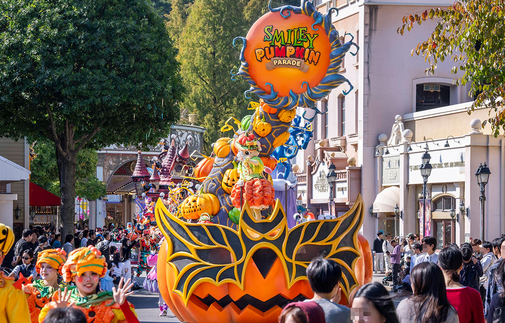 An orange pumpkin-themed float leads costumed performers along an outdoor parade route at Everland.