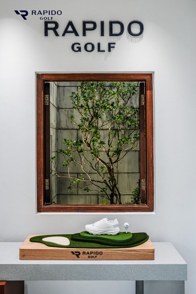 A RAPIDO GOLF shoe is displayed on a miniature putting-green stand beneath the brand’s interior signage